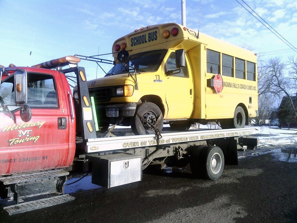 Military Towing LLC tow truck carrying school bus in Niagara Falls